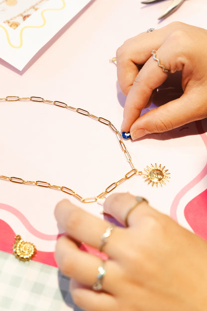Cadena dorada con charms personalizados sobre mantel rosa, taller de joyas en Vitoria